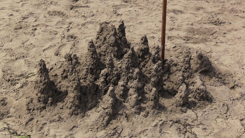 A sand sculpture of a small castle with many spires.