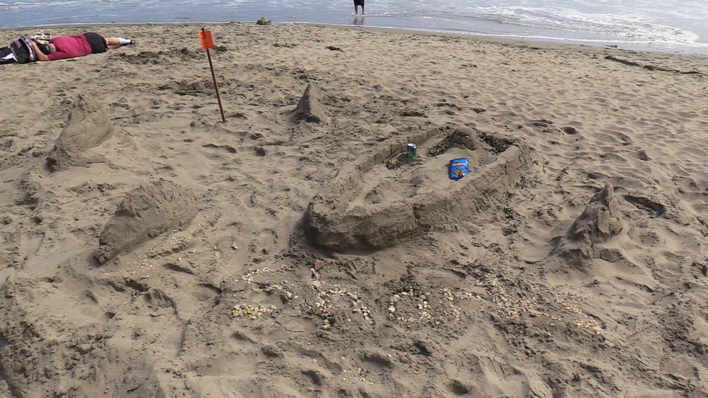 A sand sculpture of a boat surrounded by shark fins.