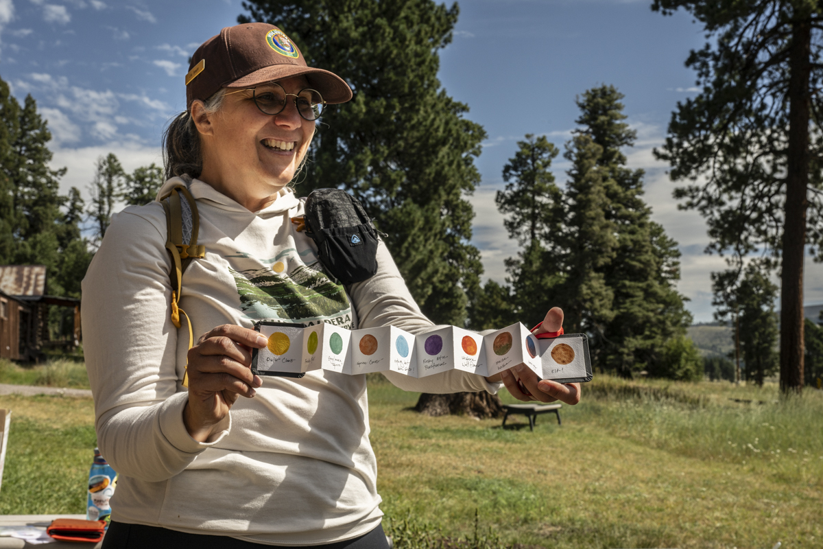 A woman holds up an accordion-folded collection of different colored circles to demonstrate watercolor paint mixing.