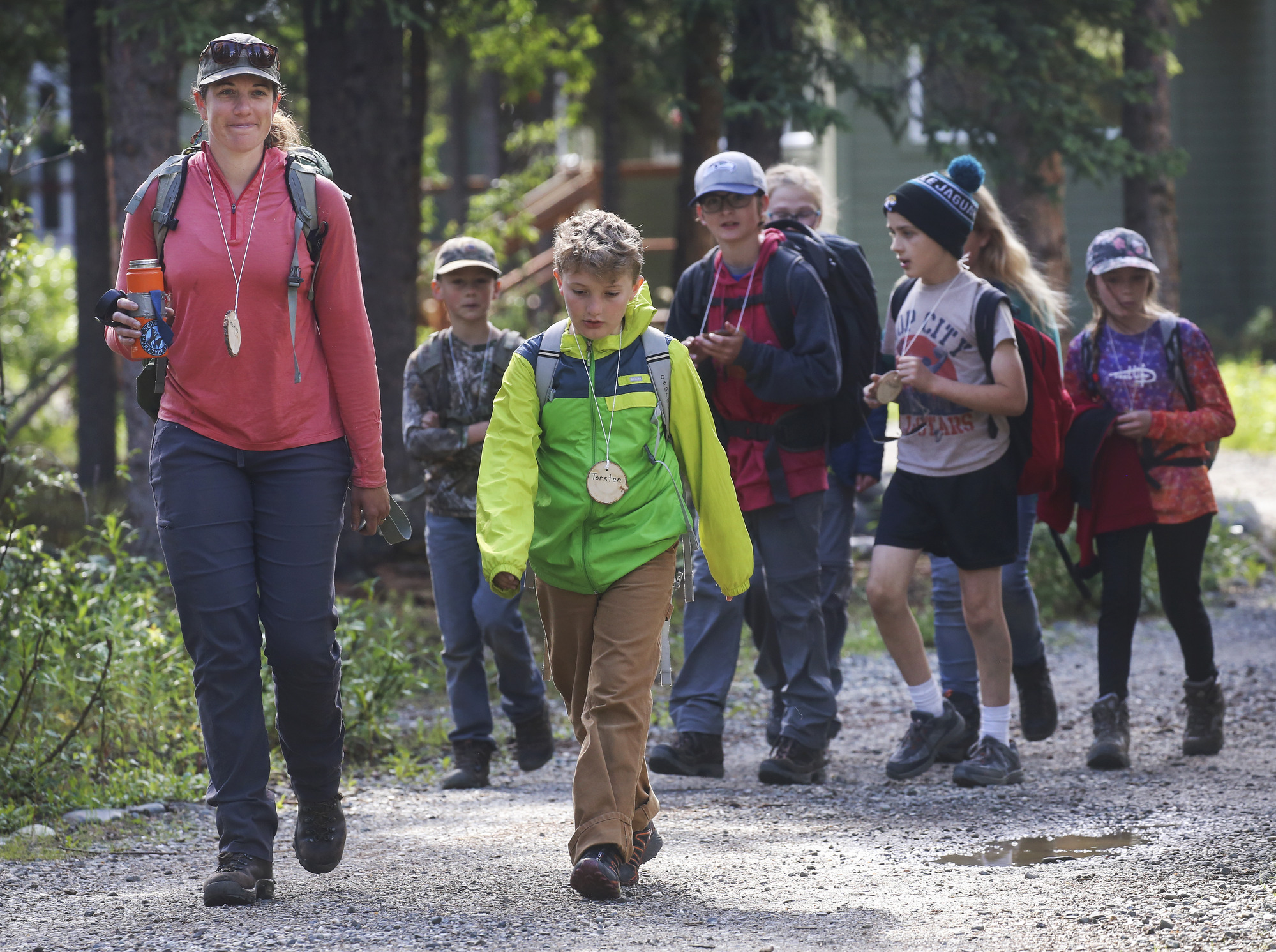 a woman leading a small group of kids down a gravel trail in a forest