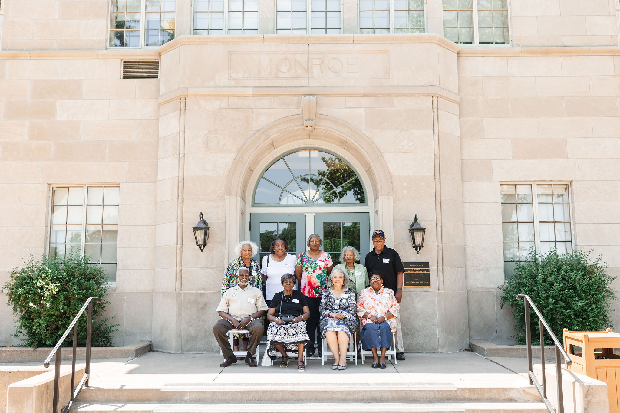 8 african american adults who are former students of Monroe Elementary School, pose infront of the School House' front doors for a class photo at the homecoming celebration.