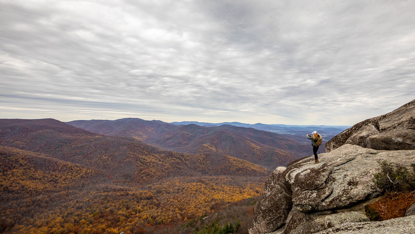 Hiker on huge boulder on right taking a photo of the valley and ridges on the left