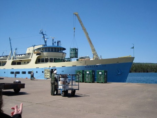 A crane on a ferry lifts a metal cage with propane tanks to put onto the deck. 