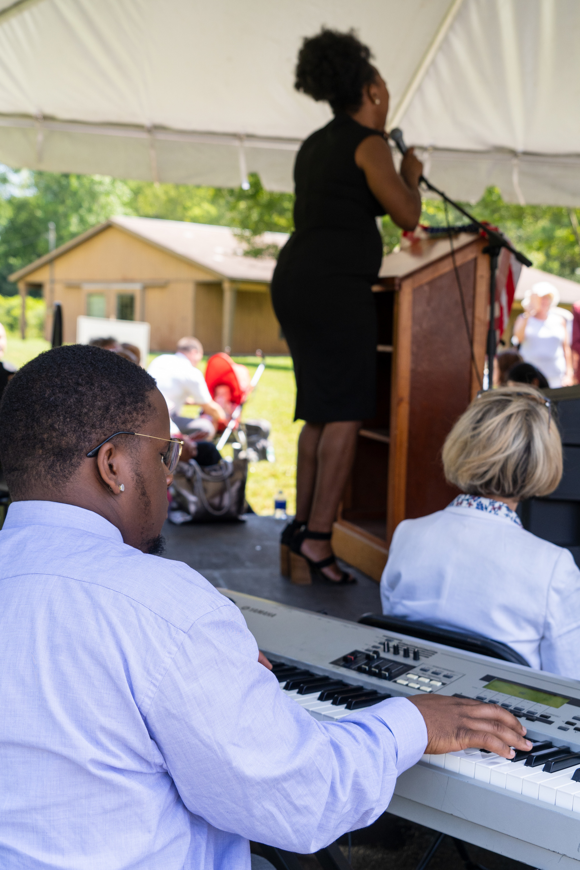 A man plays piano in front of a woman singing.
