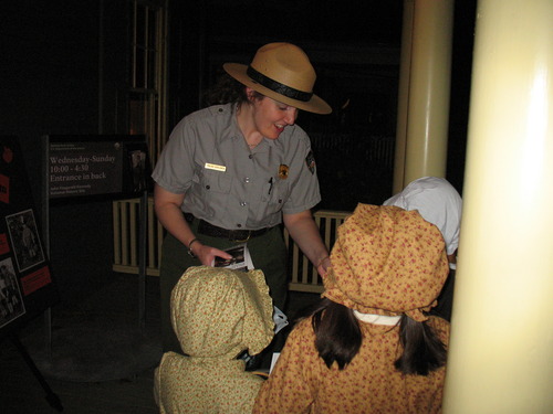 Park Ranger (facing camera) gives candy to 3 trick-or-treaters dressed in bonnets. 