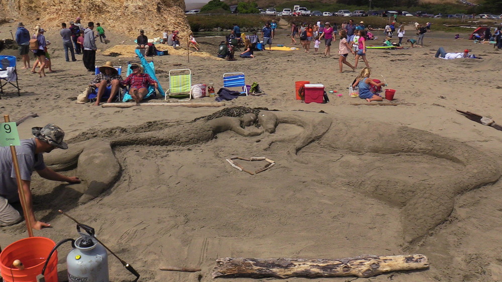 A sand sculpture of mermaid and a seahorse touching heads.