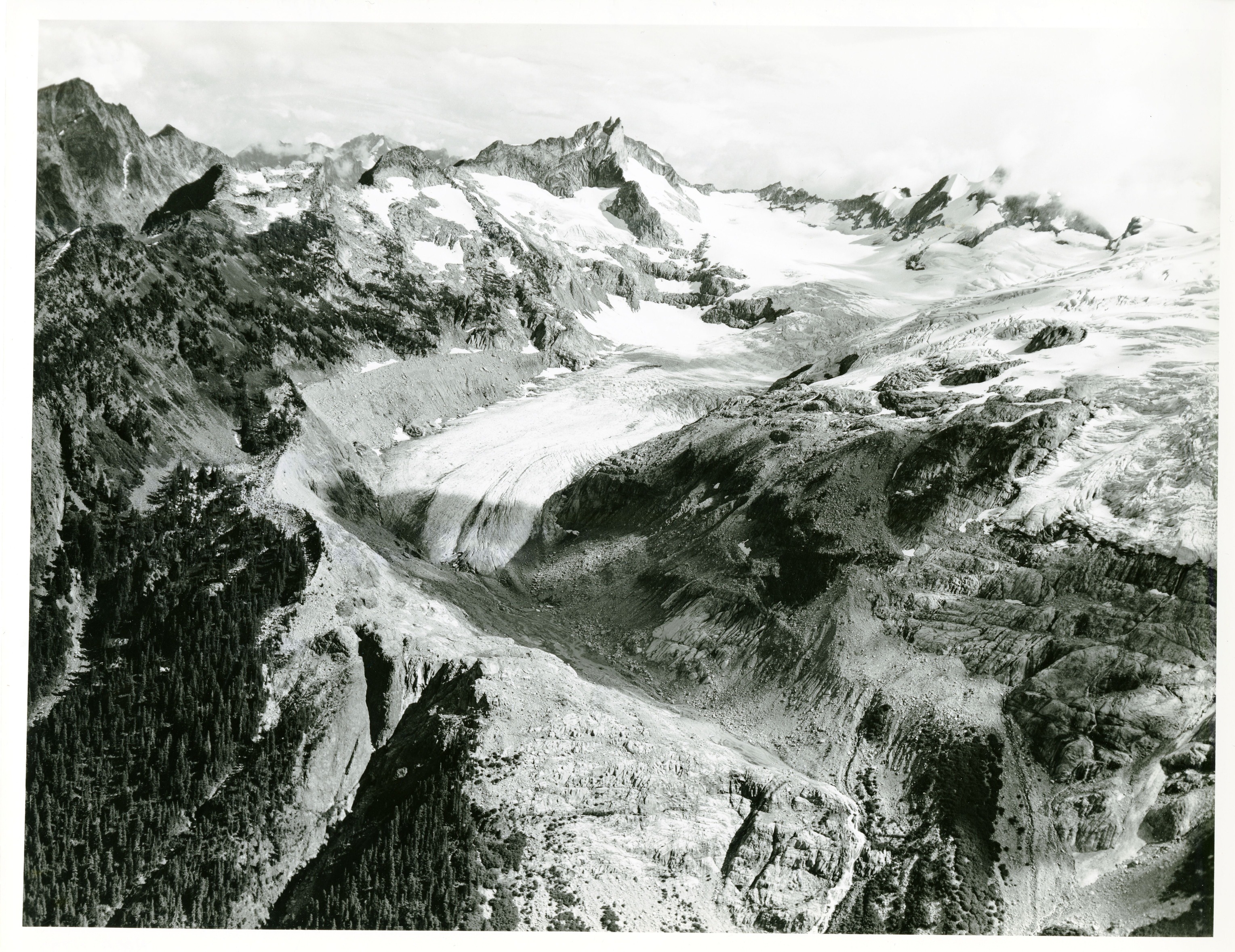 A glacier flowing down between the peaks of a mountain.