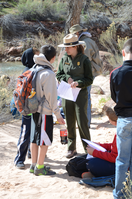 Two young schoolchildren speak with a ranger during an education program outside next to a river.