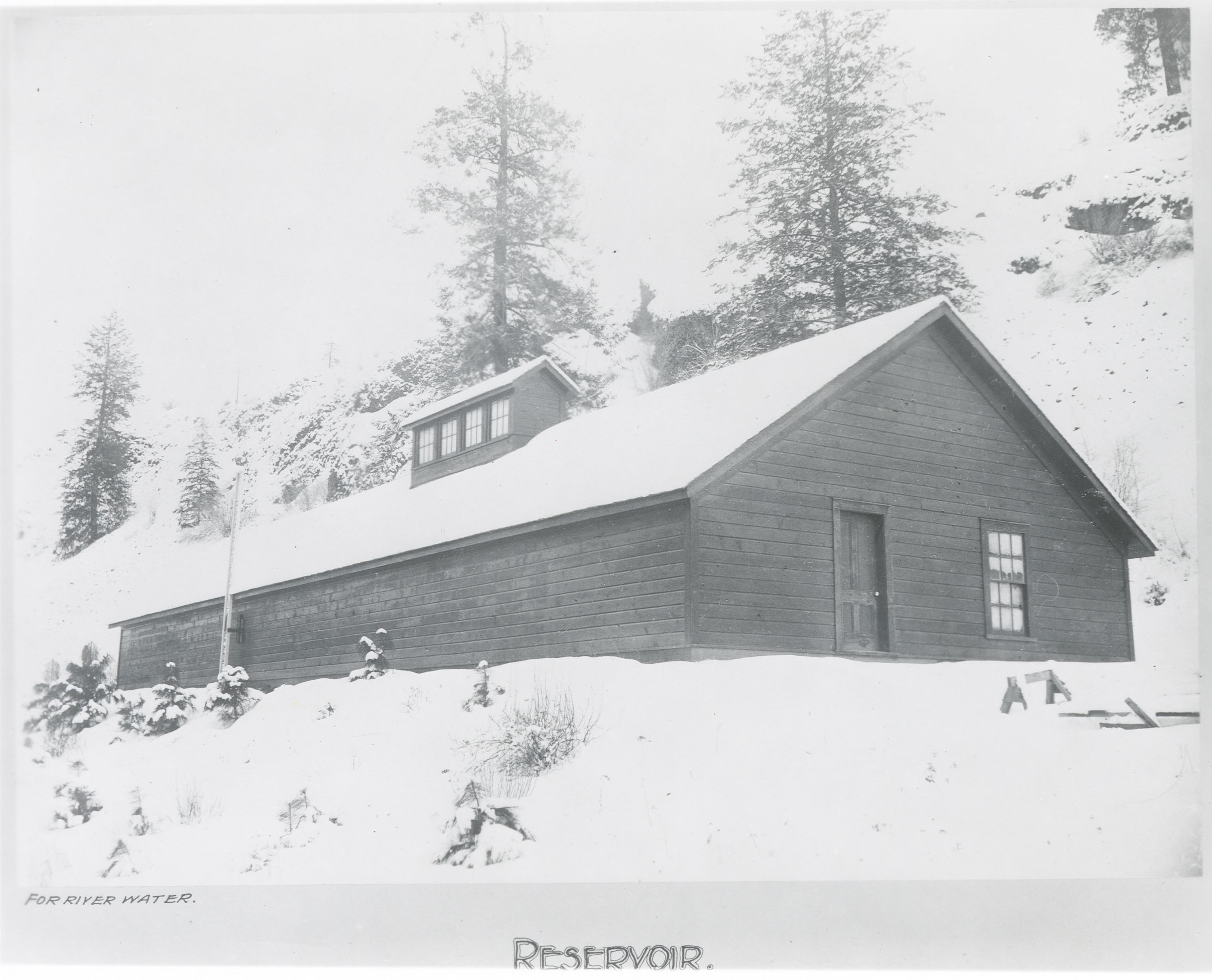 Black and white photograph of a plain wooden building in the snow