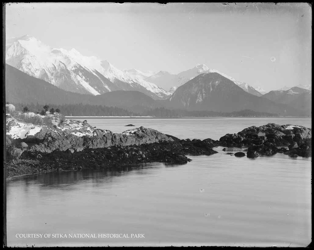 Rocky shoreline with ocean and distant mountains.