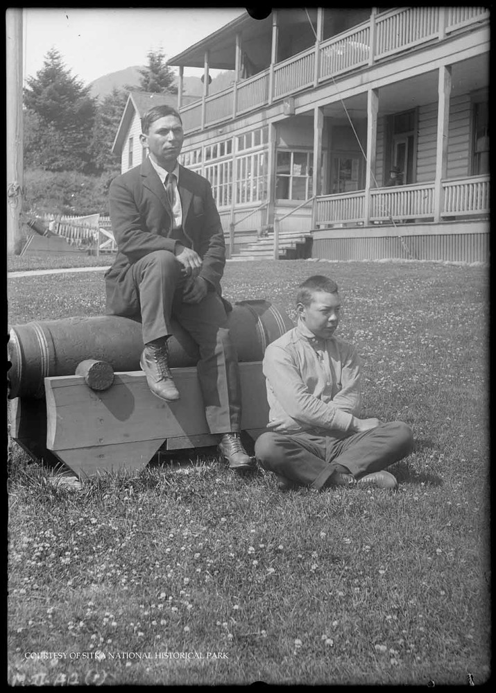 Two young men posing on a cannon in the parade grounds.