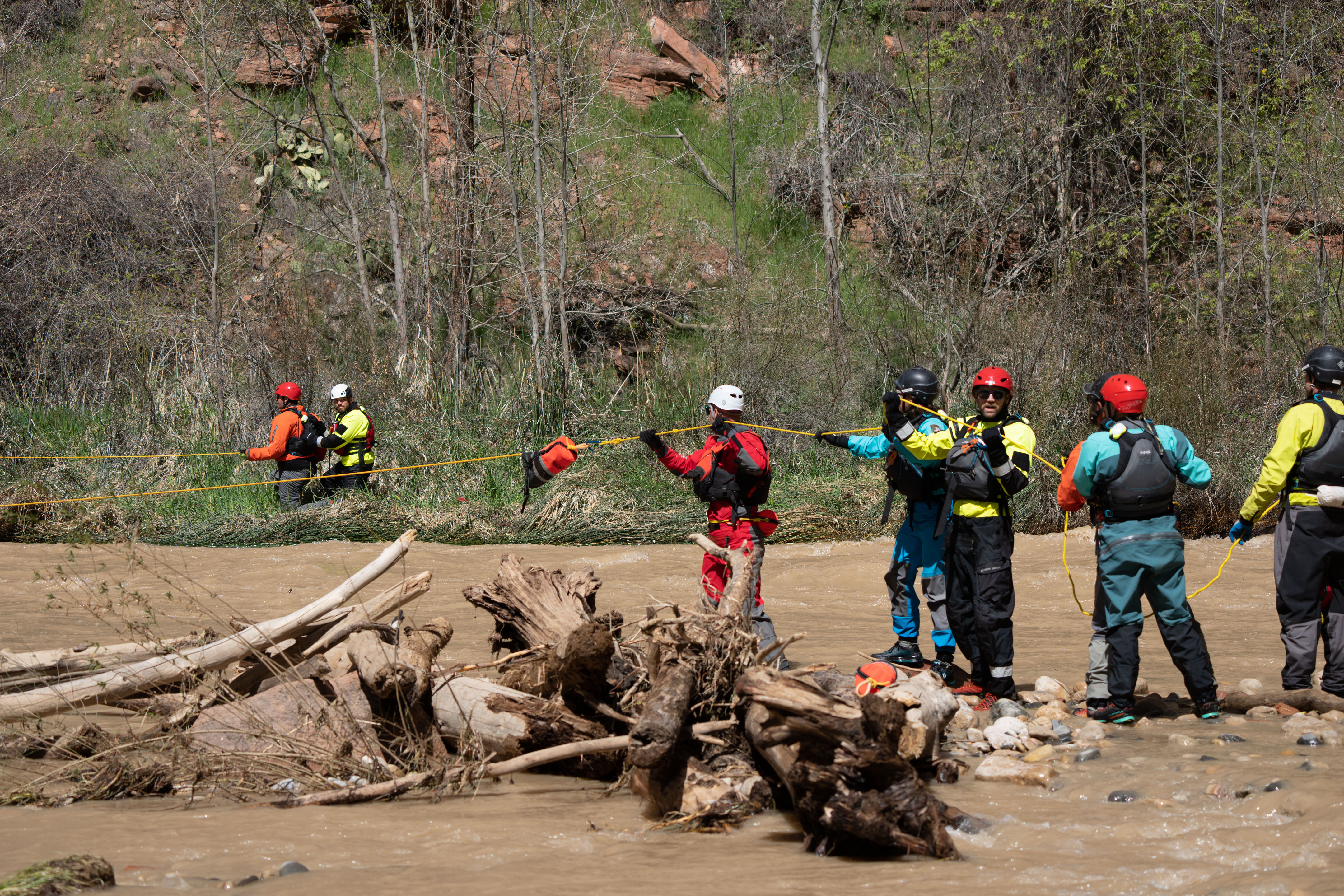 Search and rescue team members wearing bright colored dry suits, gloves and helmets hold a yellow rope on both sides of the Virgin River
