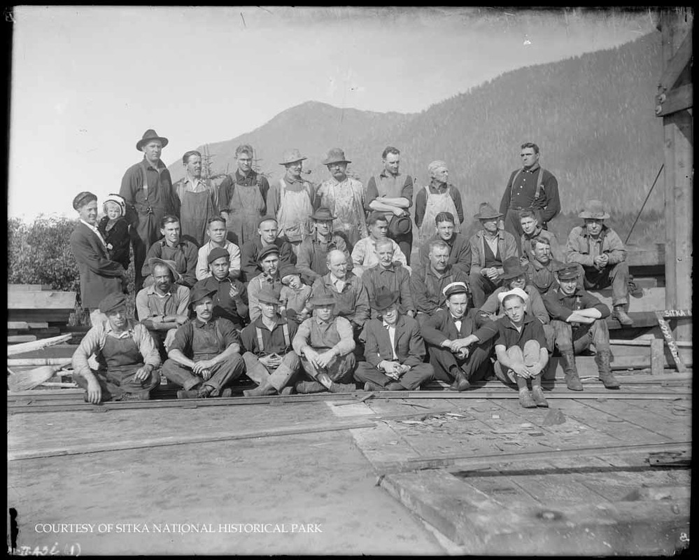 Men in work clothes with two children on a dock with milled lumber.