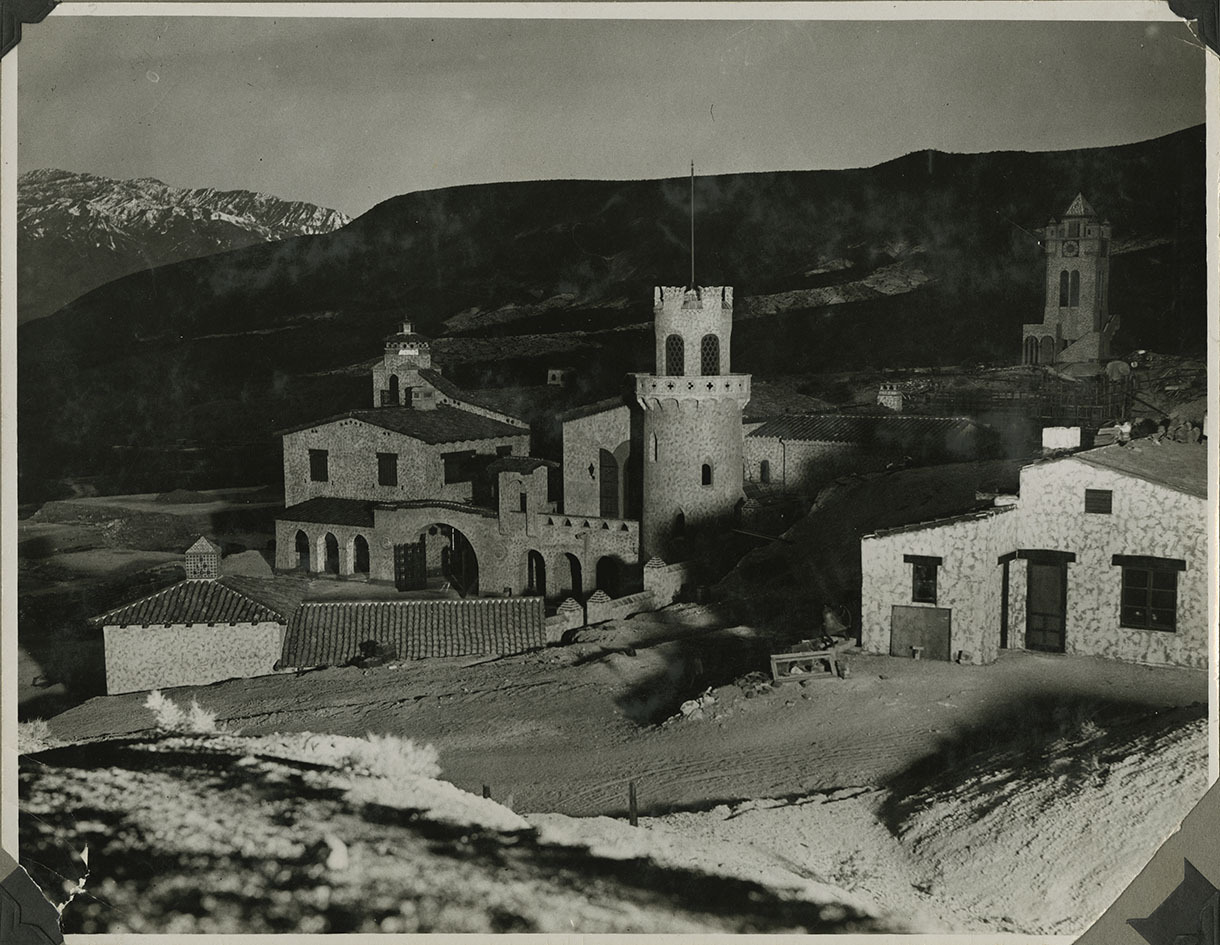 This is an historic black and white photograph from the Scotty's Castle Historic Photograph Collection, Death Valley National Park looking southwest at Scotty's Castle Gas House, Main House and Annex. Gas House and Cook House in foreground. Chimes Tower and construction of Power House and Pavilion in background. Circa 1930.