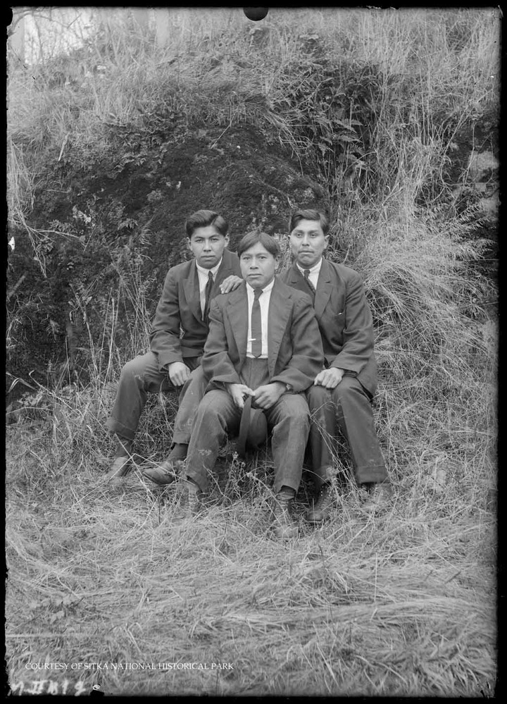 Alaska Native young men in suits and ties, standing in front of a grassy hill.