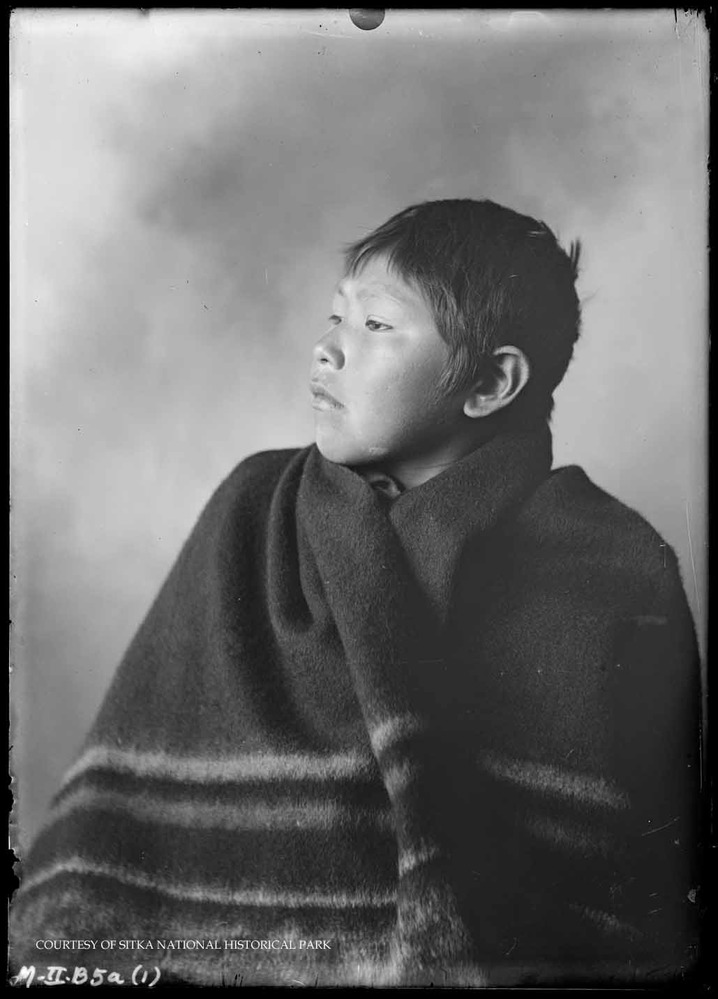 Alaska Native boy in simple dark wrap.