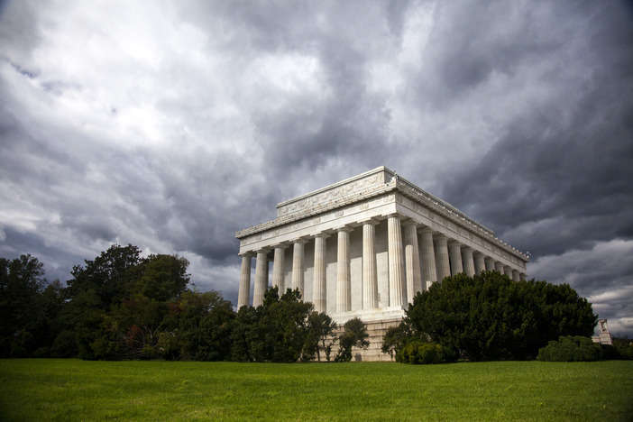 A side view of the marble Lincoln Memorial, storm clouds form above it. 