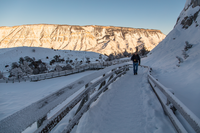 One person is walking toward the camera on a snow covered boardwalk with a flat, sunlit, mountain in the background.