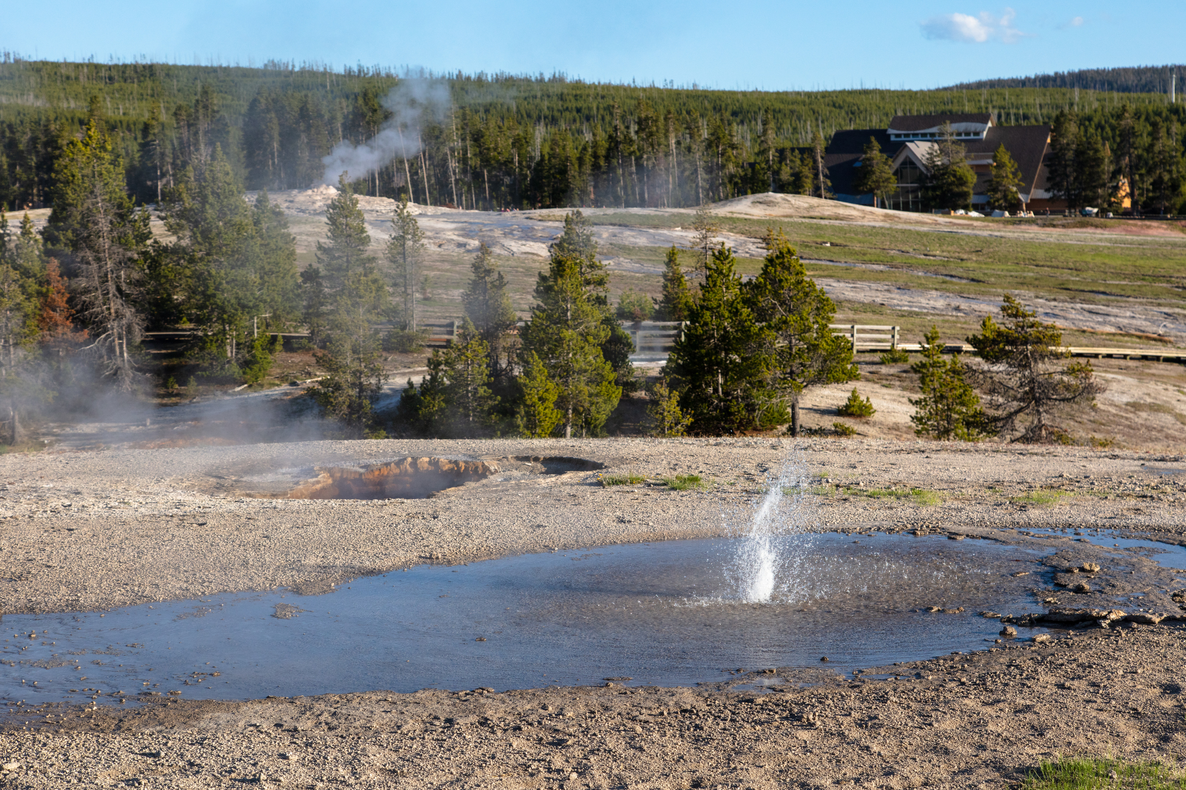 Water shoots up a couple of feet from a pool on a hill with the visitor education center in the background.