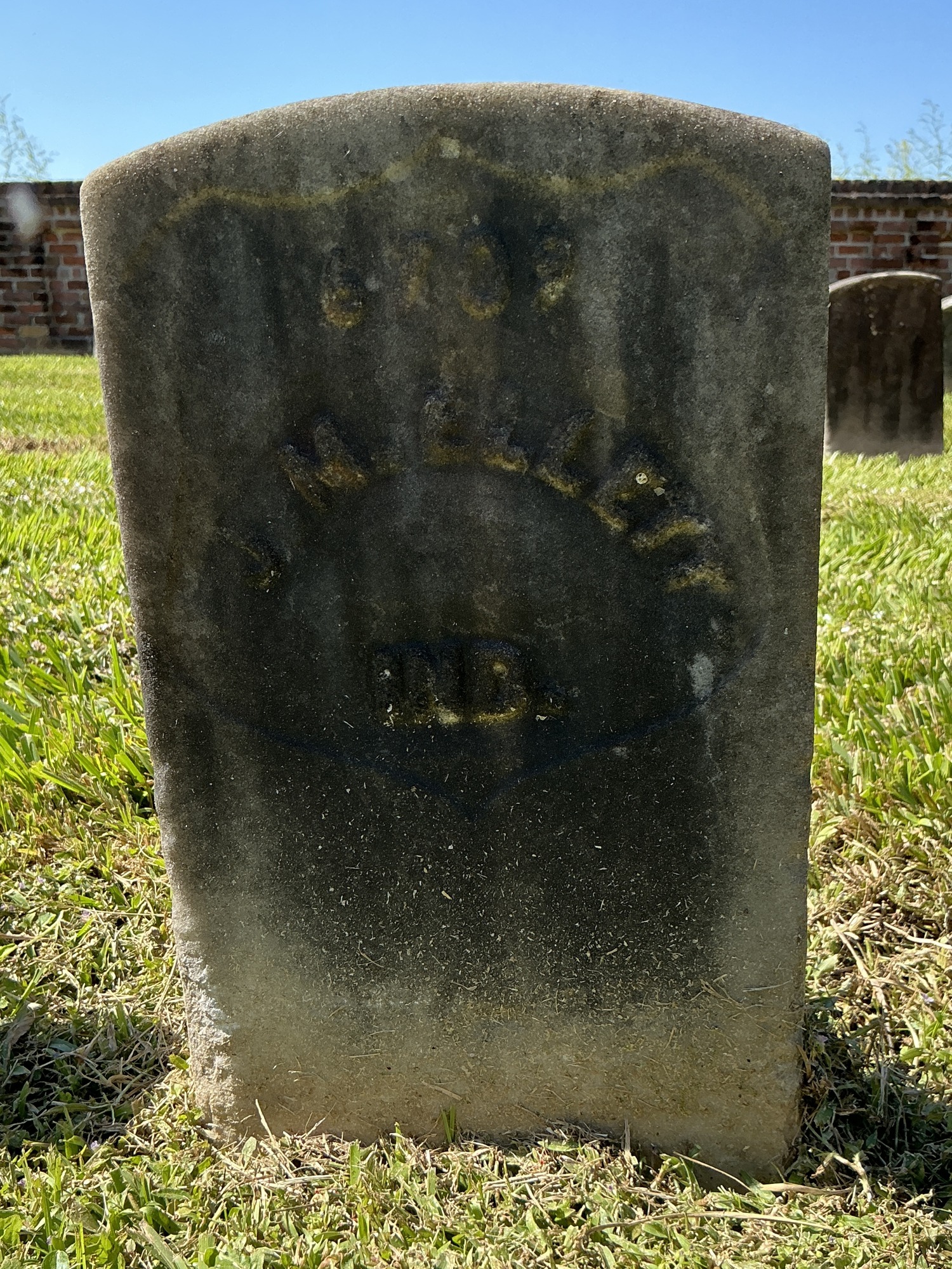 Front of historic upright marble headstone with recessed shield with recessed lettering face.