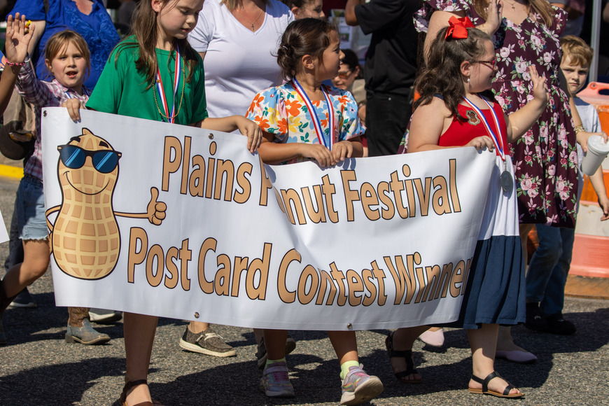 Winner of the Plains Peanut Postcard Contest walks in the Plains Peanut Festival Parade with a banner reading, "Plains Peanut Festival Contest Winners". 