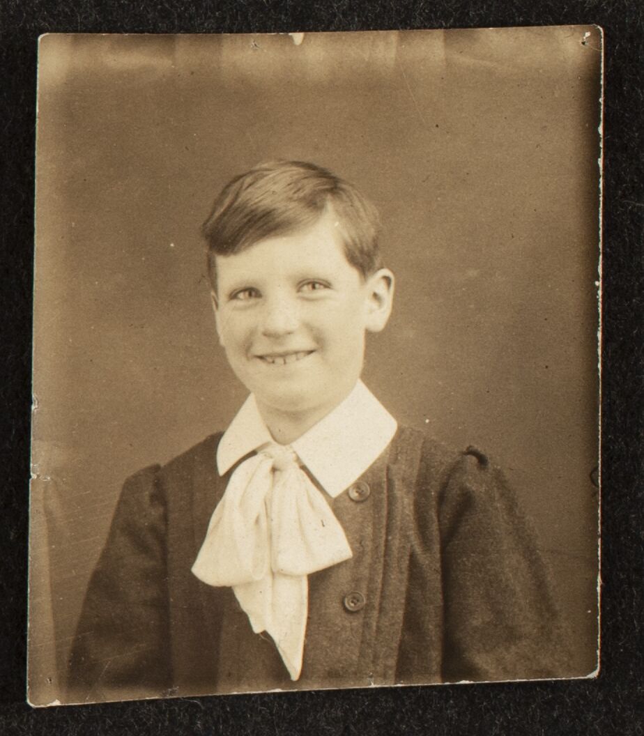 Portrait of a boy in a woolen coat with a large floppy bowtie.