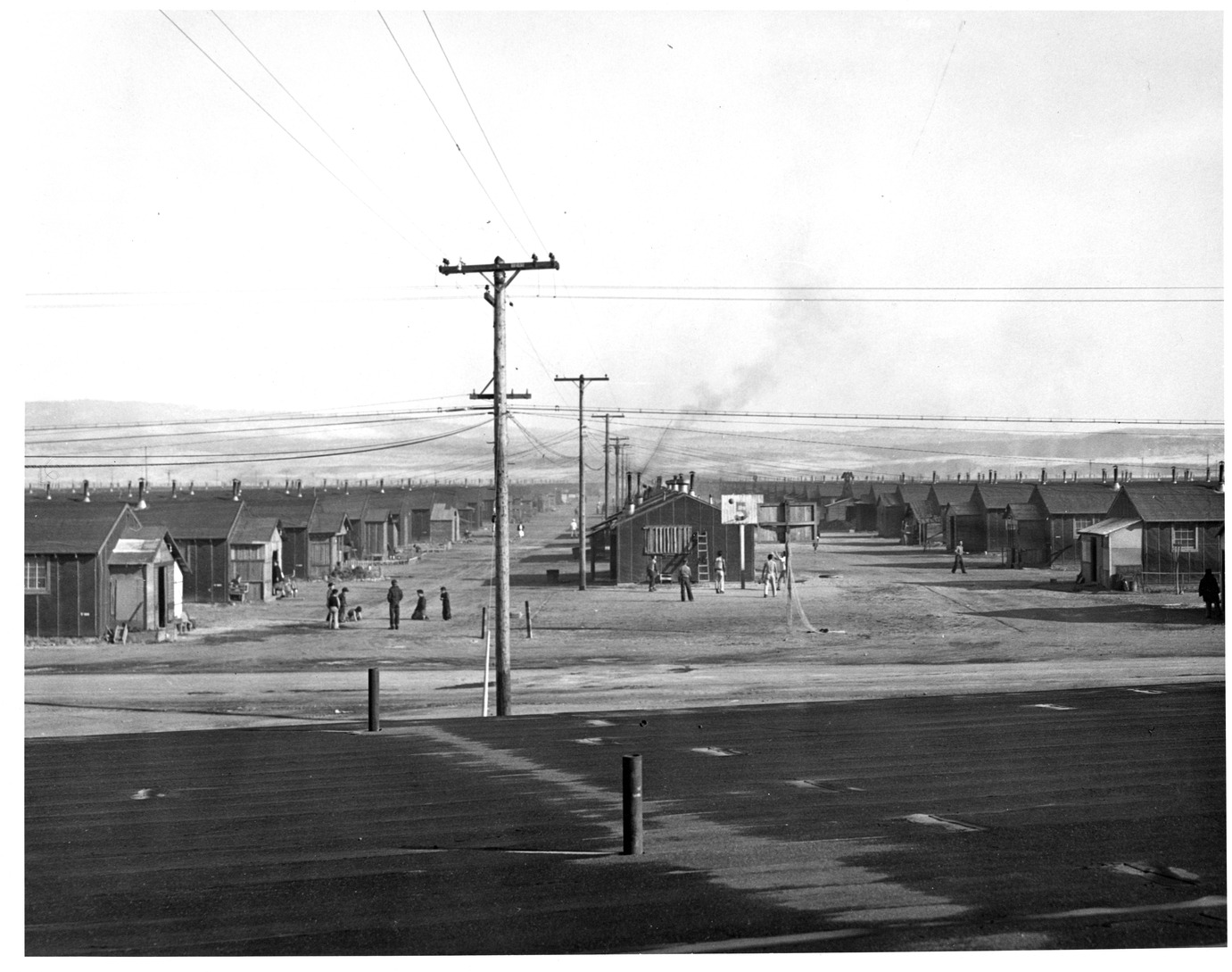 A group of children play basketball at the end of a row of uniform wood buildings, some of which have porch additions. Nearby, another group play marbles.