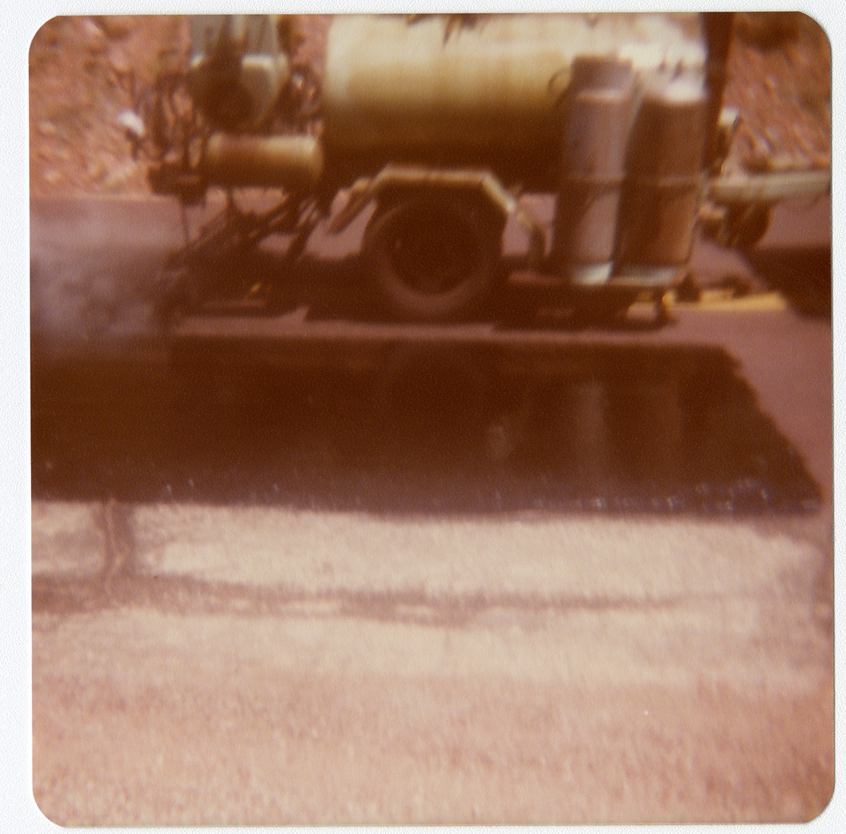 Section of road after chipsealing with close up of chipsealing vehicle.