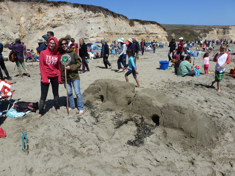 Two women standing to the left of a sand sculpture of the Roman Bridge of Zamora, Spain.