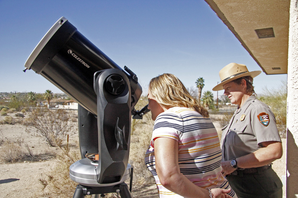 Visitor peers through a telescope while ranger stands behind her