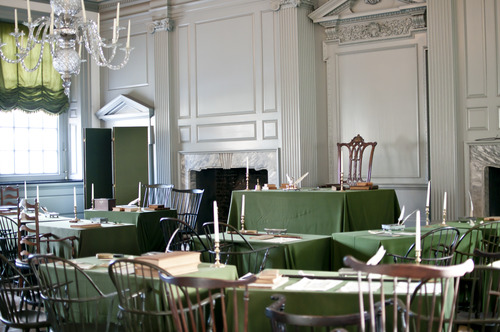 Color image showing room filled with wooden chairs and green baize-covered tables. 