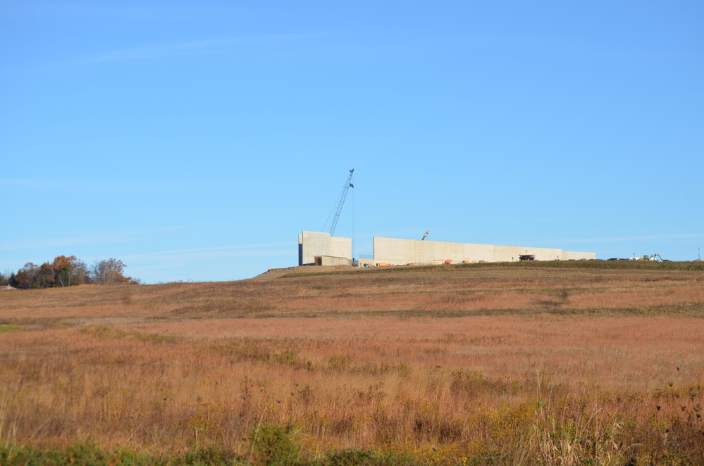 Tall gray concrete walls running along a ridge with a break in the walls.  Blue sky above.