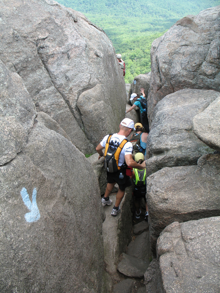 Hikers walk down a narrow rock rift on Old Rag