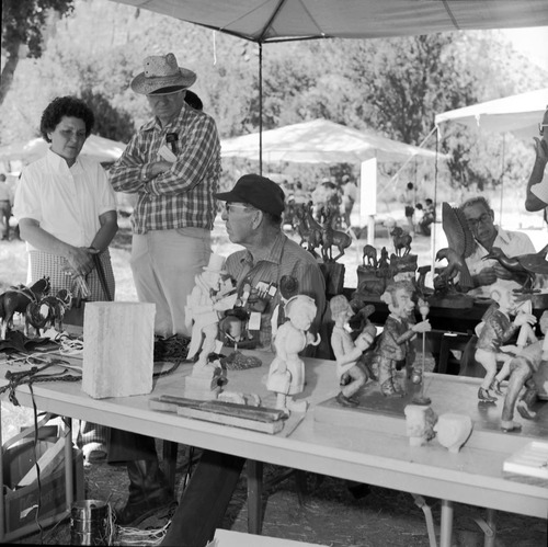 Man demonstrating carving and talking with visitors at the third annual Folklife Festival in Zion National Park, September 1979. Leo Fesler in background with his carvings.
