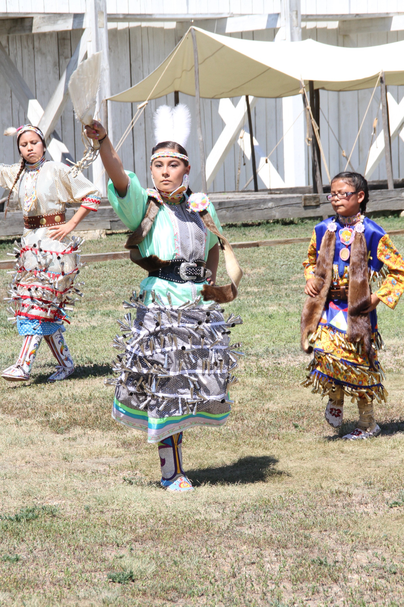 Three girls in traditional American Indian dress consisting of skirts covered in tassels dancing