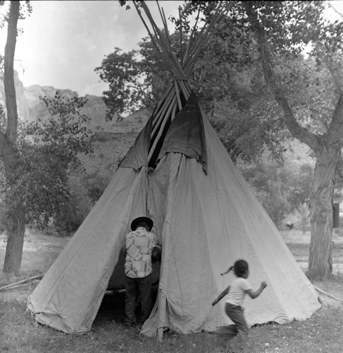 Clifford Jake demonstrates setting up a tipi while girl runs past him at the first annual Folklife Festival, Zion National Park Nature Center, September 1977.
