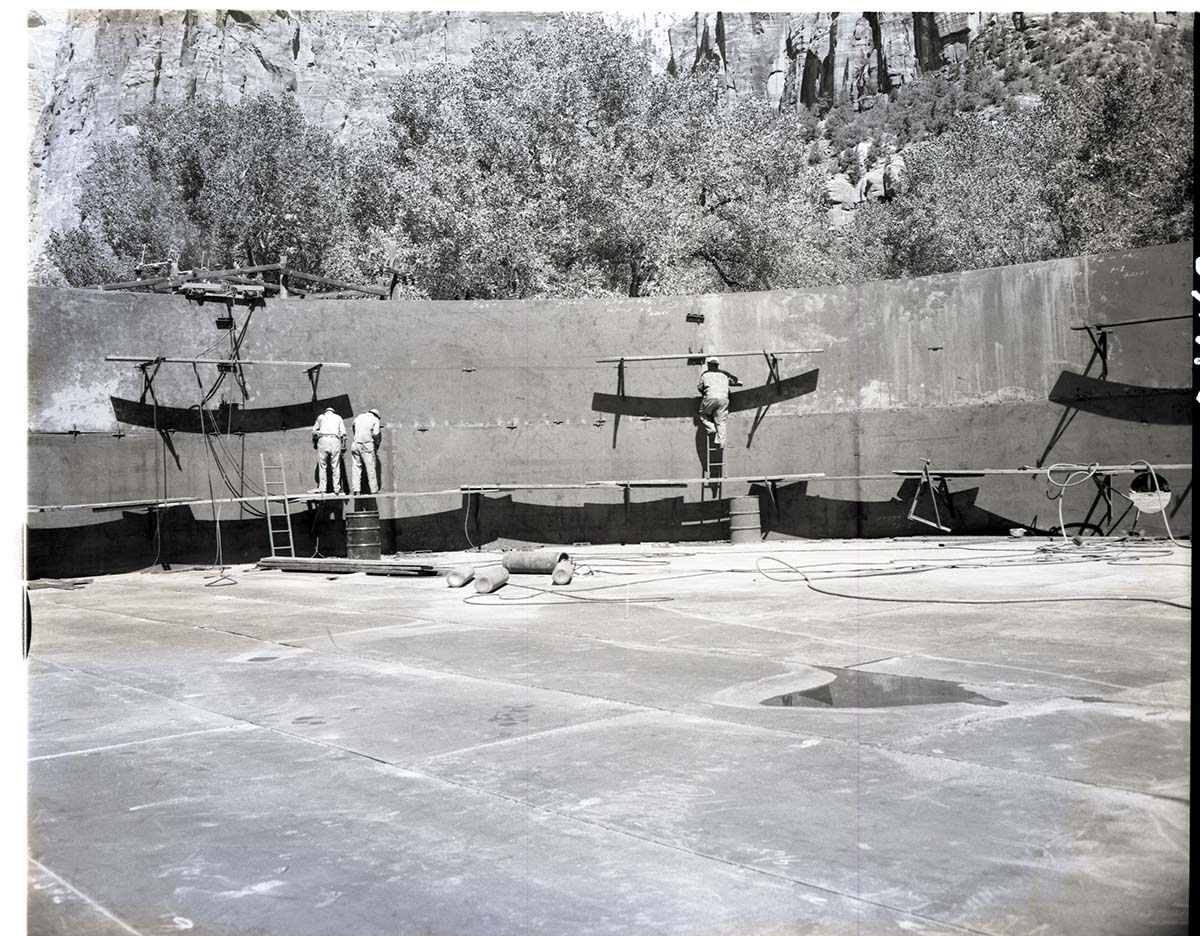 Construction of million gallon water tank at Birch Creek with workmen placing sections of wall.