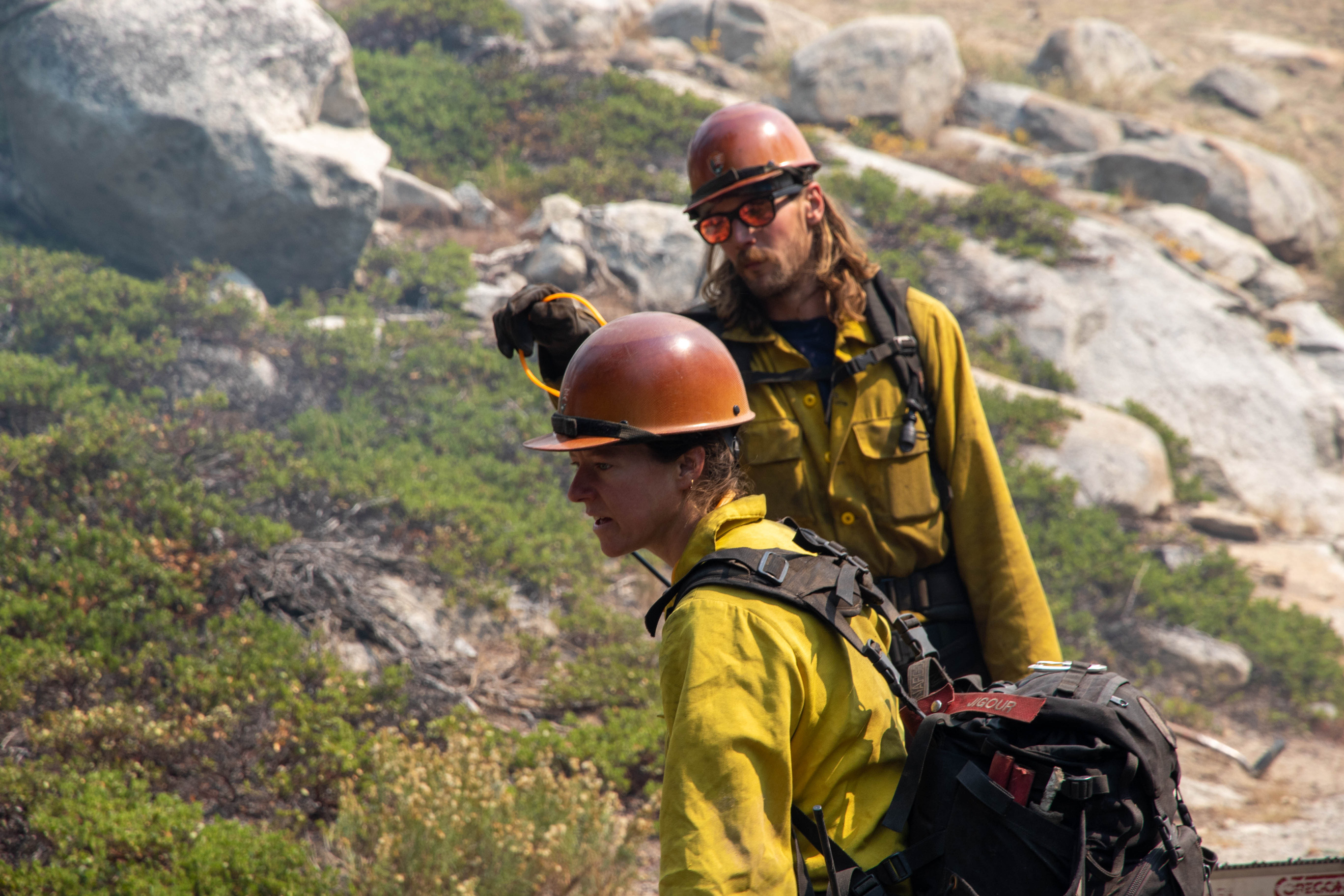 Wildland firefighters walk through wooded areas with smoke and fire around them