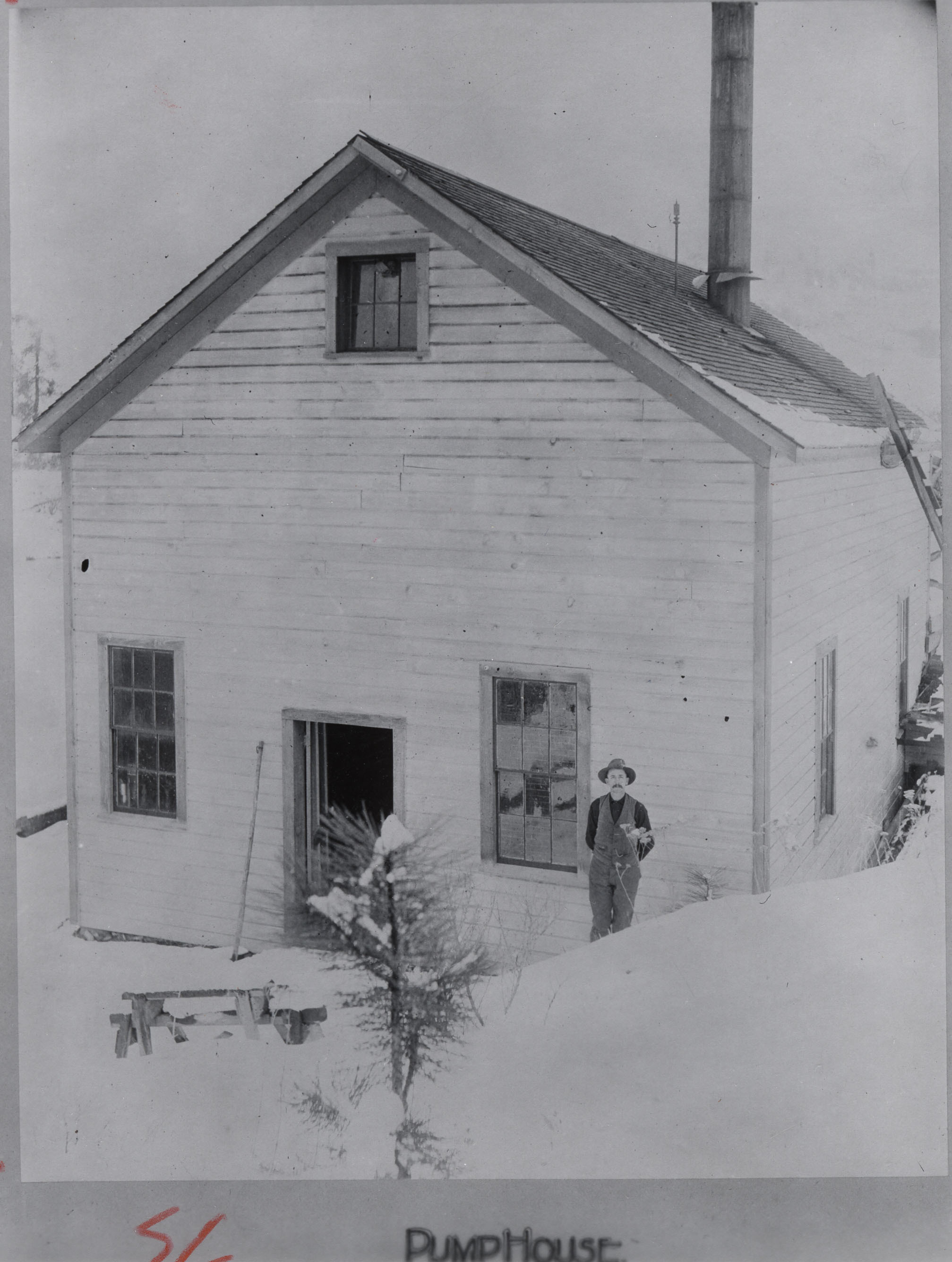 Black and white photograph of a man standing in front of plain two story wooden building