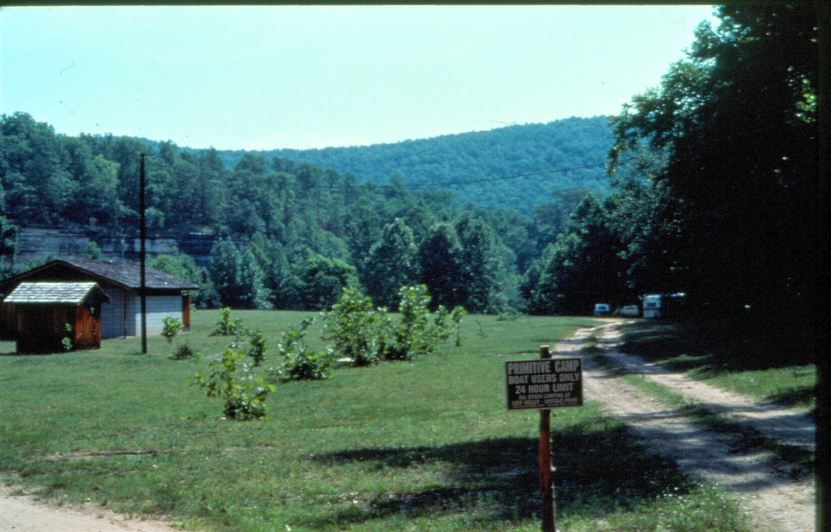 color photo with road at right, field at center and trees in background.