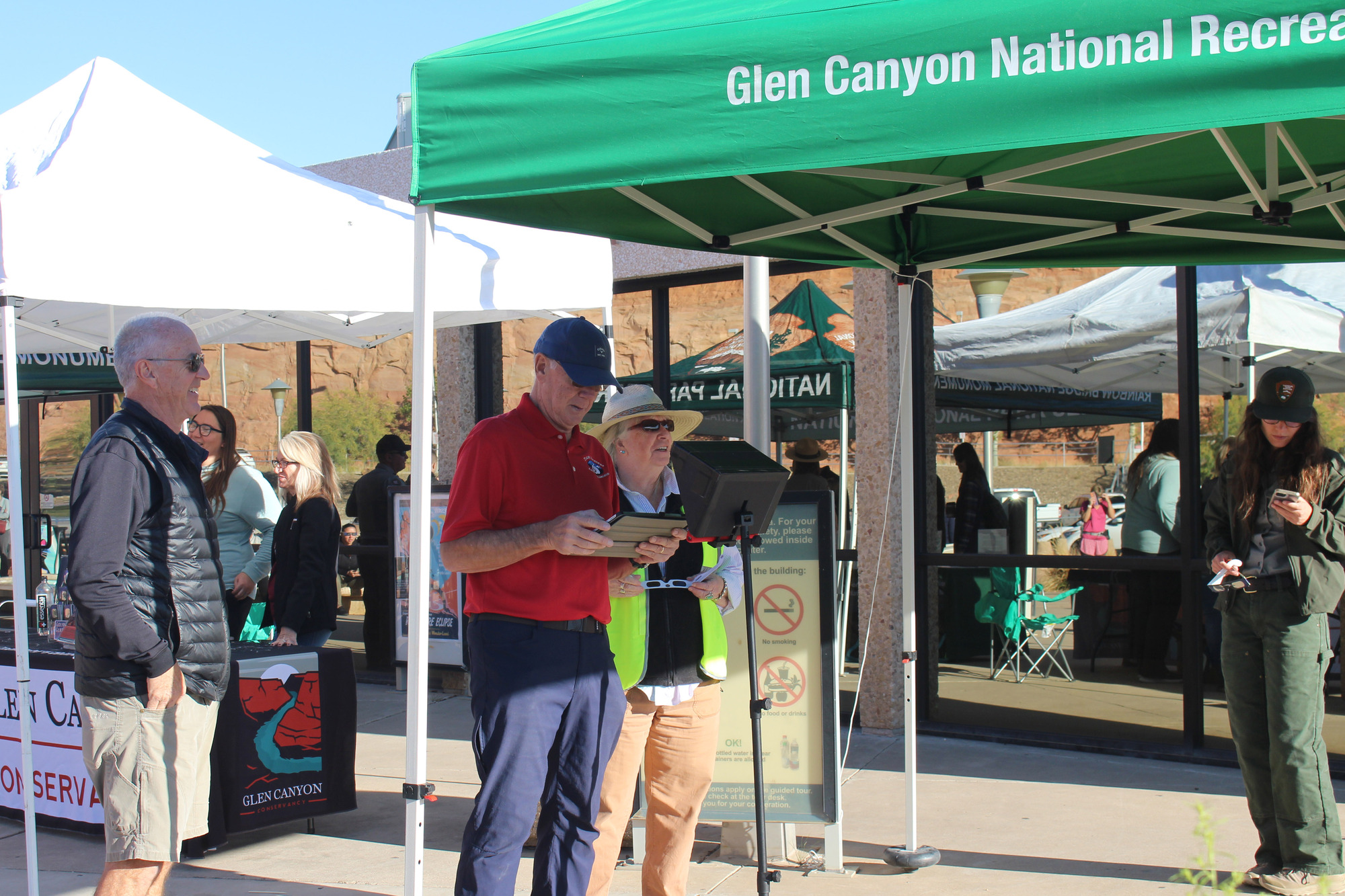 Park rangers and others hold computer equipment while standing under a pop-up tent that reads, "Glen Canyon National Recreation Area."
