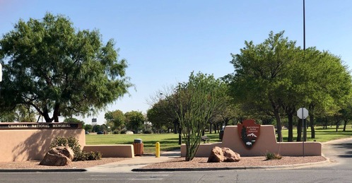 Low stucco walls bear signs, one with words "Chamizal National Memorial," the other a large National Park Service arrowhead logo. Trees and open grassy area are in the background.