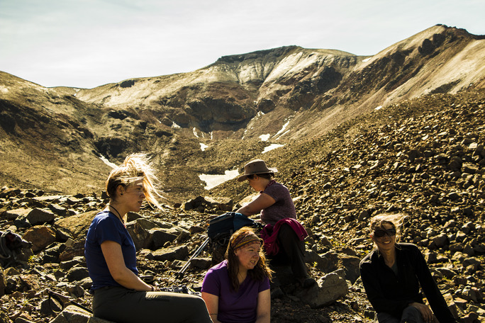 four women sitting down on a talus slope near a mountain top