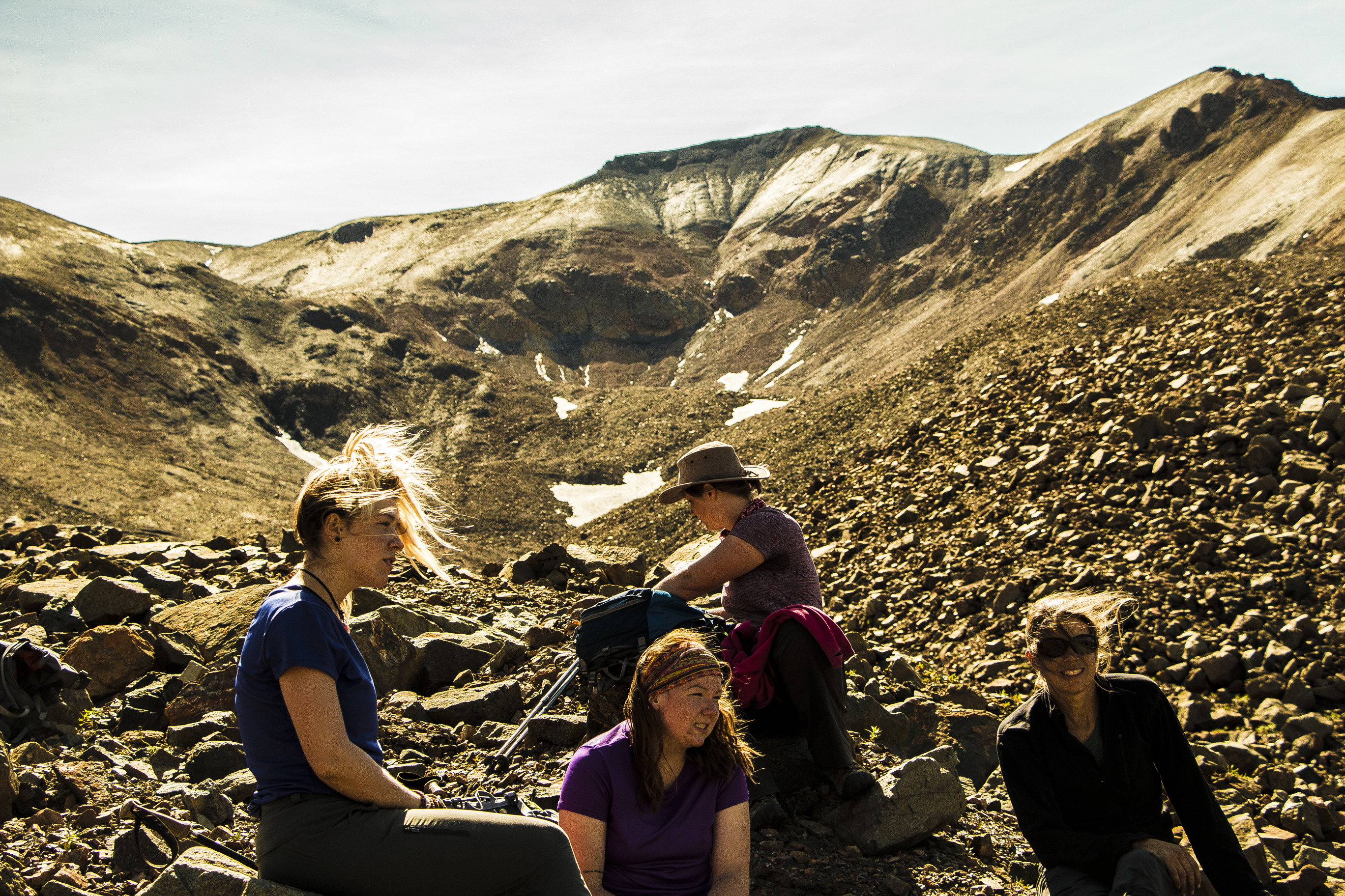 four women sitting down on a talus slope near a mountain top