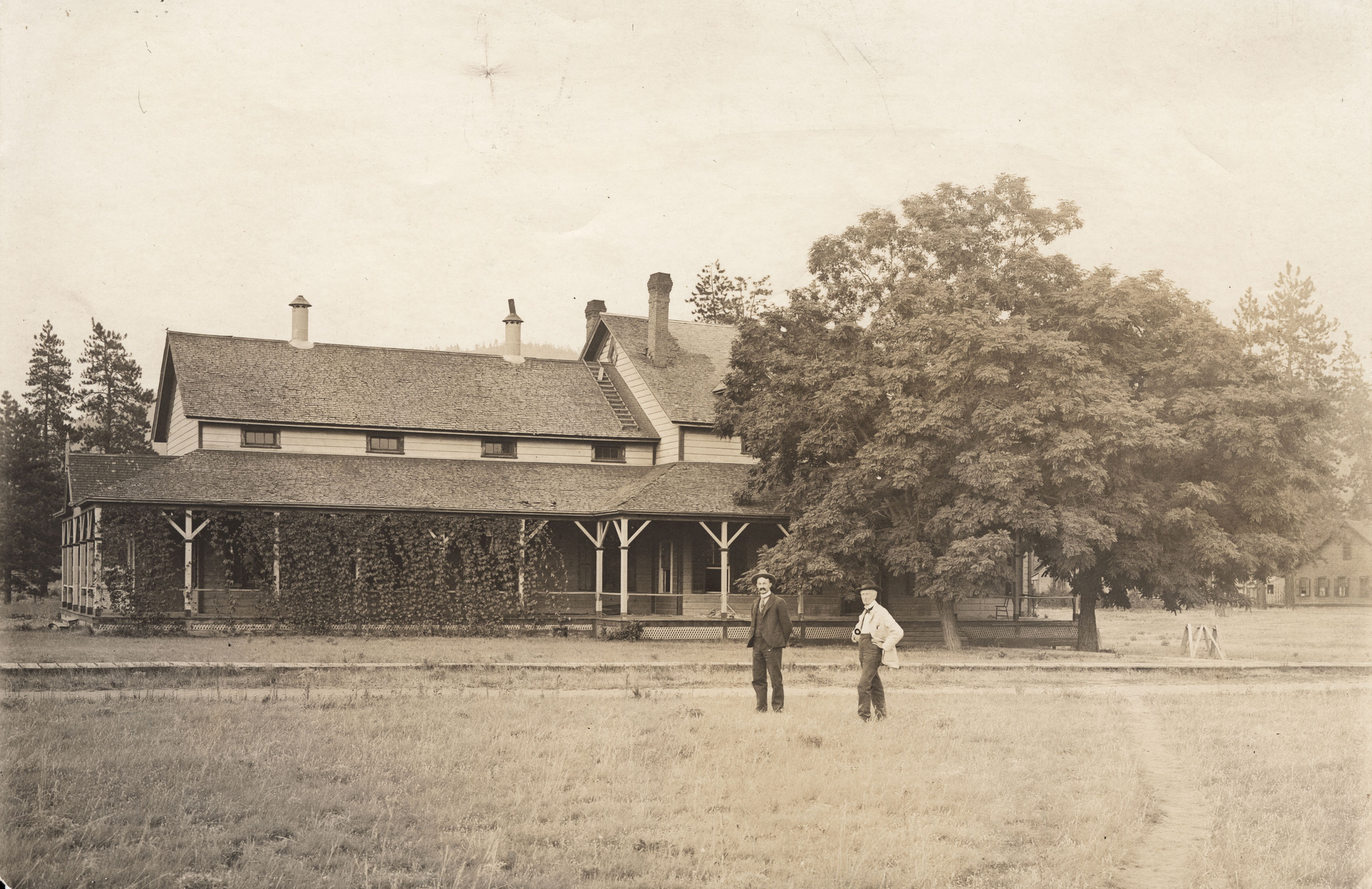 Black and white photograph of two men standing front of a two story building