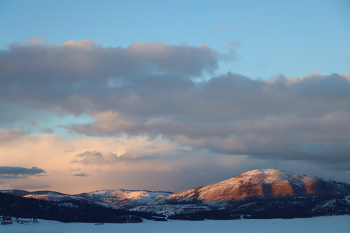 Early evening light illuminates a distant, rounded peak covered in snow.