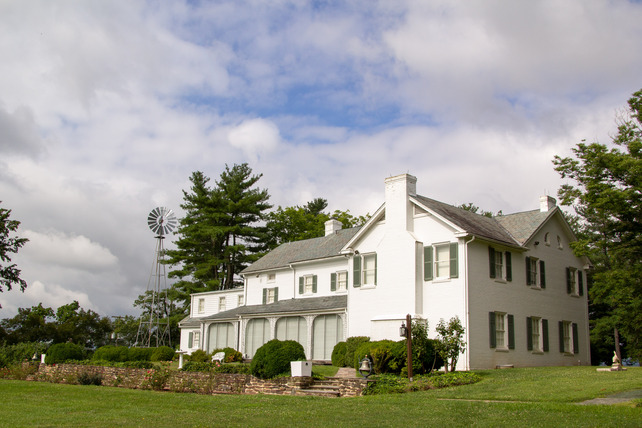 A two story white house with green shutters and manicured lawn.