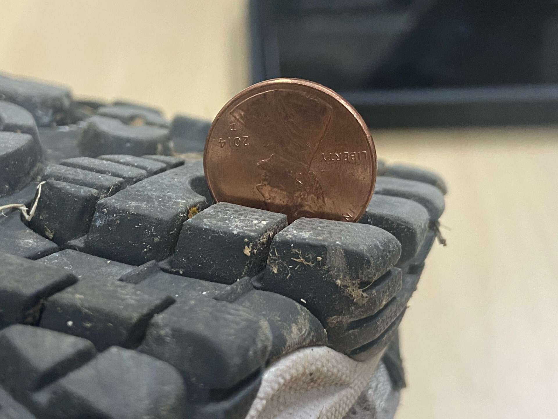 Close up of sole of boot with penny sticking out of tread. 