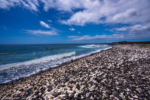 A rock beach of white coral and black lava rock with small waves coming ashore