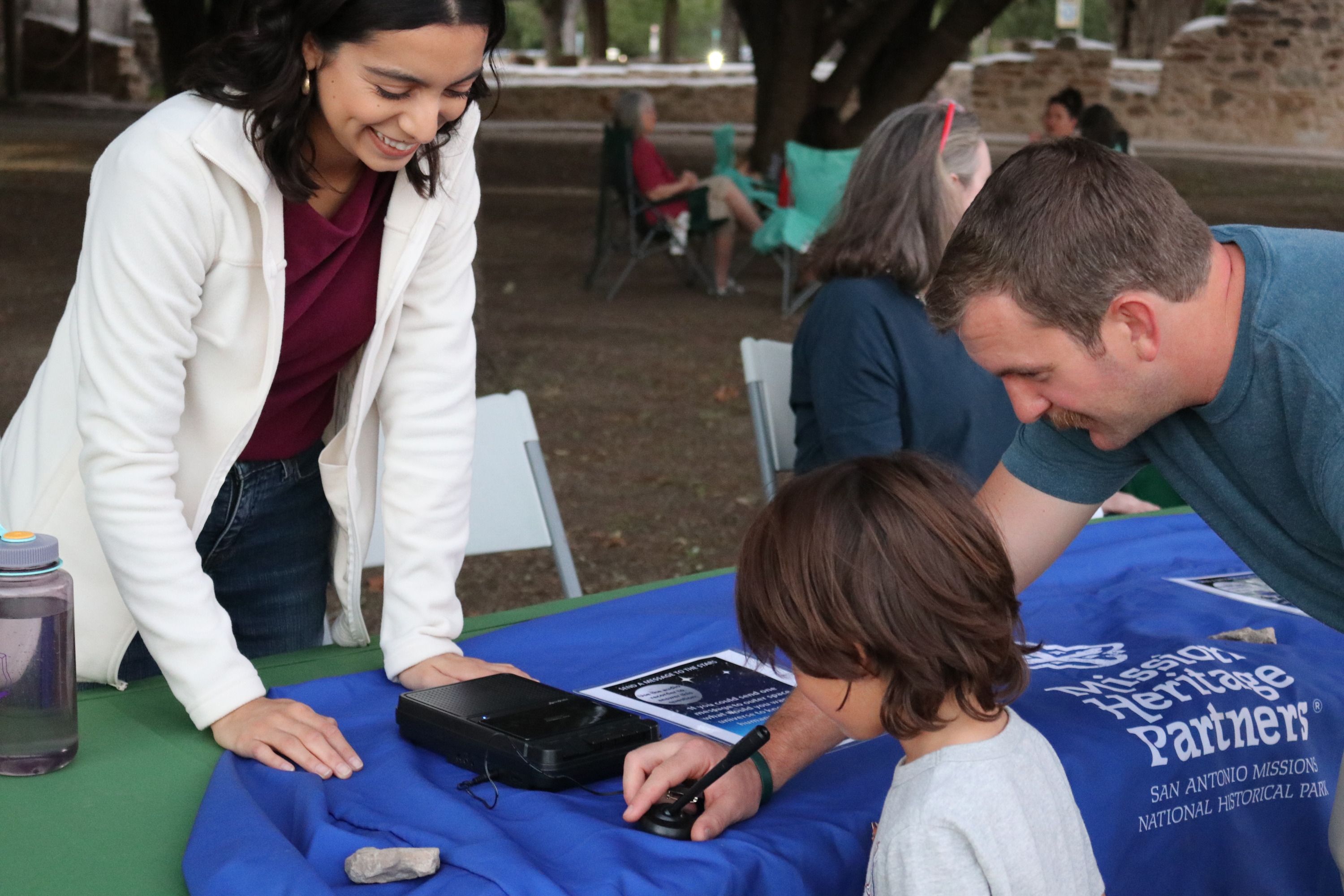 Young child records their voice on a tape recorder with the help of an adult. 